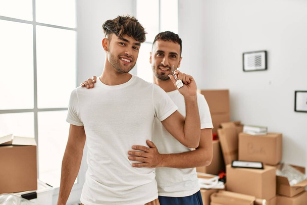 Zwei hispanische Männer umarmen sich und halten Schlüssel für neues Haus in der neuen Heimat in den Händen - Foto, Bild