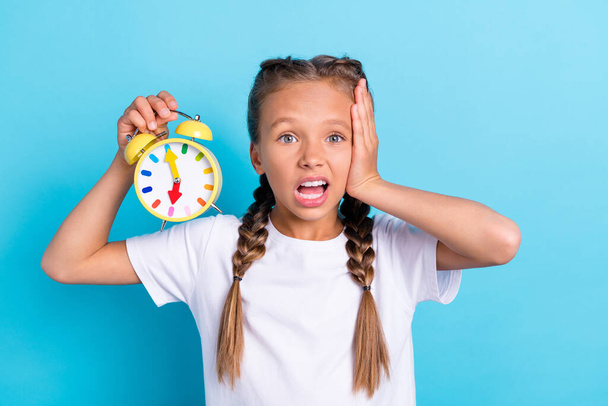 Photo of young little girl amazed shocked omg hold clock time late missed isolated over blue color background. - Fotó, kép