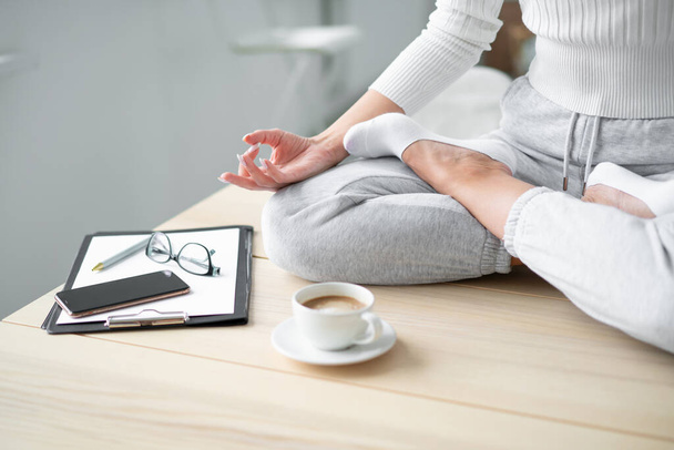 Closeup of a seated young woman's hand in a lotus position at the desktop with a cup of coffee. - Photo, image