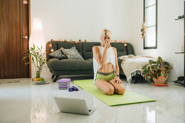 Blonde woman sitting on a floor and training by online course looking in laptop. - 写真・画像