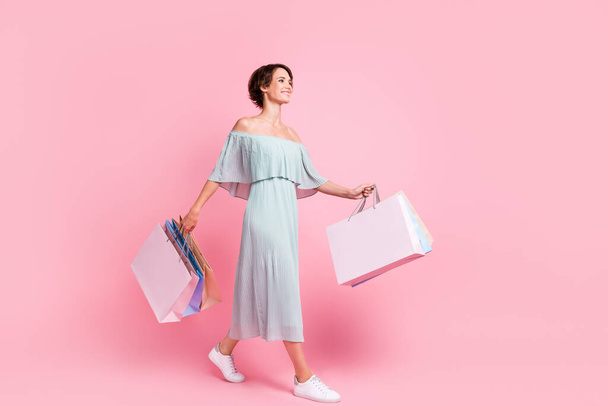 Full size profile side photo of young girl go walk look empty space hold bags shopper sale isolated over pink color background. - 写真・画像