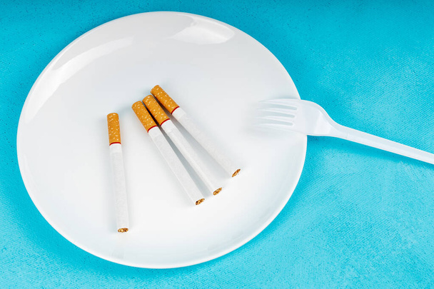 vier Zigaretten auf einem Teller und eine Einweggabel aus Kunststoff. Anstatt zu essen, Nikotinsucht zu bekämpfen - Foto, Bild