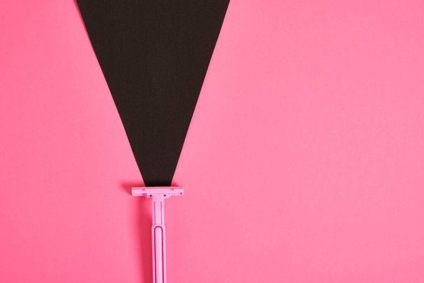 a pink plastic disposable razor and a black triangle made of paper on a pink background, an association on the theme of feminism and shaving hair from a female body - Zdjęcie, obraz