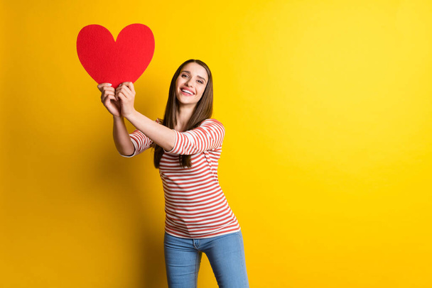 Portrait of attractive cheerful girl holding big large heart card having fun isolated over bright yellow color background. - Foto, Bild