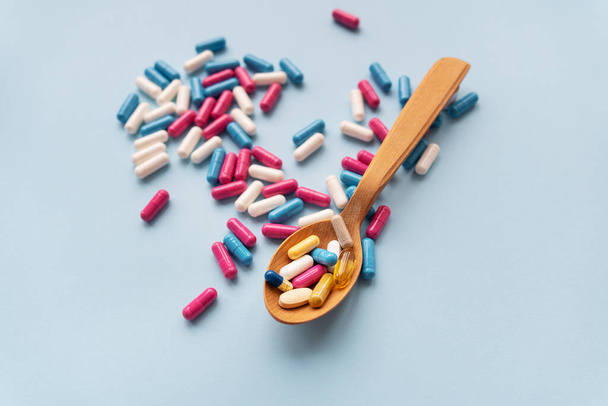 Varias pastillas sobre un fondo azul junto con una cuchara de madera en la que las vitaminas - Foto, Imagen