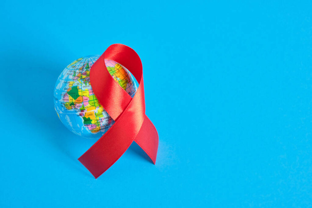 World AIDS day. The symbol of solidarity is a red ribbon nd toy globe ball blue background 1st december world aids day - Zdjęcie, obraz