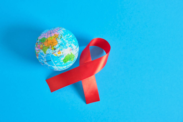 World AIDS day. The symbol of solidarity is a red ribbon nd toy globe ball blue background 1st december world aids day - Φωτογραφία, εικόνα