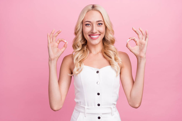 Photo of funny charming young woman dressed white overall smiling showing okey signs isolated pink color background. - Foto, Bild