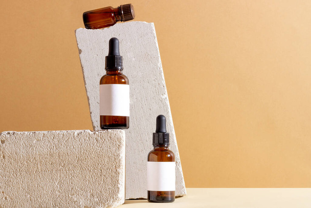 Face and body skin care products in a glass bottle with a pipette on a concrete podium. Cosmetics for women with natural ingredients. Copy space, layout - Valokuva, kuva