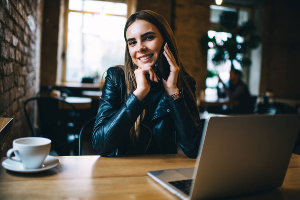 Portret wesołej kobiety copywriter uśmiecha się do kamery, dzwoniąc do kolegi w celu omówienia treści publikacji na blogu internetowym, szczęśliwy biały freelancer z laptopem korzystających z telefonu komórkowego - Zdjęcie, obraz