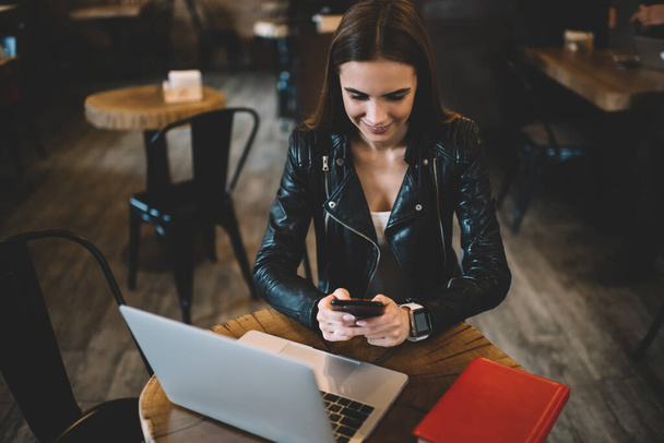 Millennial blogger connecting to internet for sharing media content during smartphone networking, happy skilled freelancer using netbook and cellphone technologies for chatting and web messaging - Fotó, kép