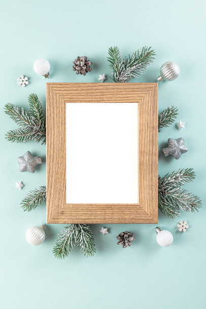 Christmas or Happy New Year blank photo frame with fir tree branches, holiday decorations on blue background. Flat lay. Mock up. Top view. Vertical orientation - Photo, Image