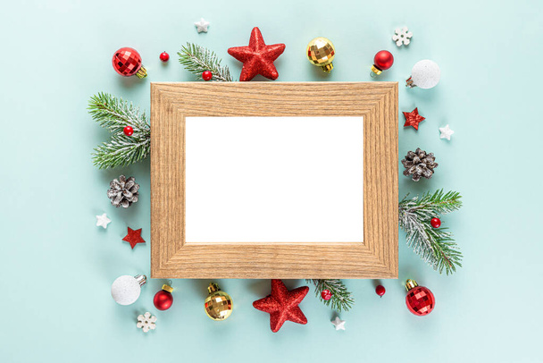 Blank Christmas photo frame with fir tree branches, holiday decorations on blue background. Mock up. Flat lay. Top view - Photo, Image