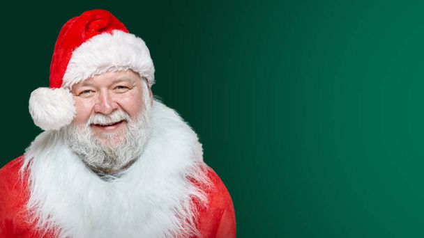 Closeup image of a happy Santa Claus dressed in a red coat and a hat, isolated green background. Space for text. - Photo, Image