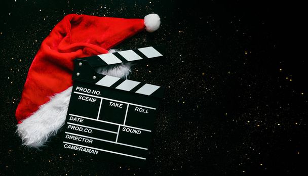 Movie πλακέτα με καπέλο του Αϊ Βασίλη και αφρώδη glitter με χώρο για κείμενο σε μαύρο φόντο. Χριστουγεννιάτικες ταινίες - Φωτογραφία, εικόνα