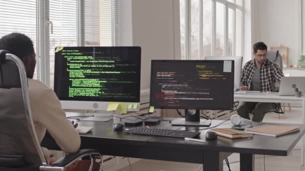 Stab shot van team van programmeurs zittend op werkplekken voor computer monitoren met lopende programmacodes op schermen in modern kantoor - Video