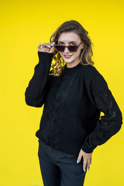 pretty young girl posing in a black warm sweater near the yellow wall - Фото, зображення