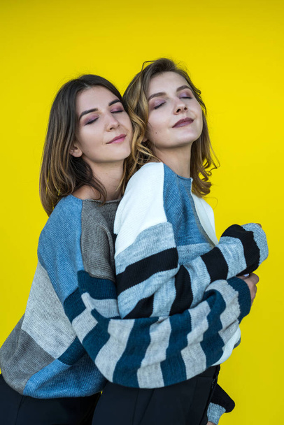 young girlfriends posing together in modern knitted sweaters isolated on yellow wall studio portrait - Foto, Imagen