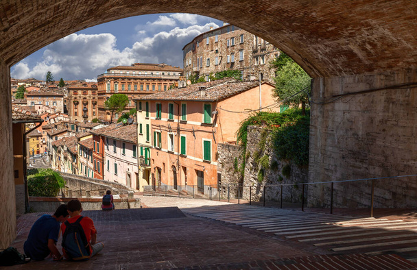 Perugia, Umbria, İtalya. Ağustos 2021. Tarihi merkezin muhteşem manzarası: antik su kemeri renkli evlerin gözden kaçırdığı muhteşem bir gezinti alanı. Güneşli bir gün, insanlar gölgede oturuyor.. - Fotoğraf, Görsel