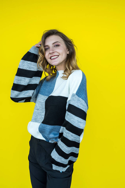 vrij lachende vrouwelijke posign in het dragen van gebreide trui geïsoleerd op gele kleur achtergrond - Foto, afbeelding