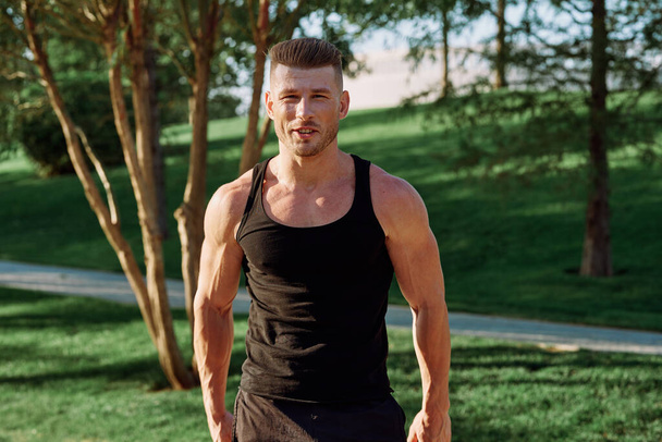 athletic man in black t-shirt with dumbbells in the park training - Fotografie, Obrázek