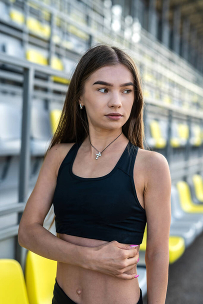Young woman in sportwear is sitting on a stadium chair and resr after morning exercise - Fotografie, Obrázek
