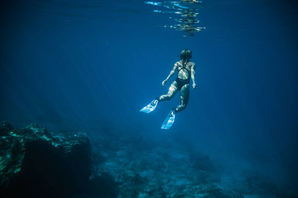Underwater shooting girl dives underwater freediving in a black swimsuit in clear water - 写真・画像