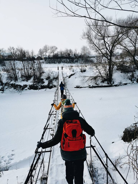A Group of hiking tourists is going over the river bridge. Winter View. - Photo, Image