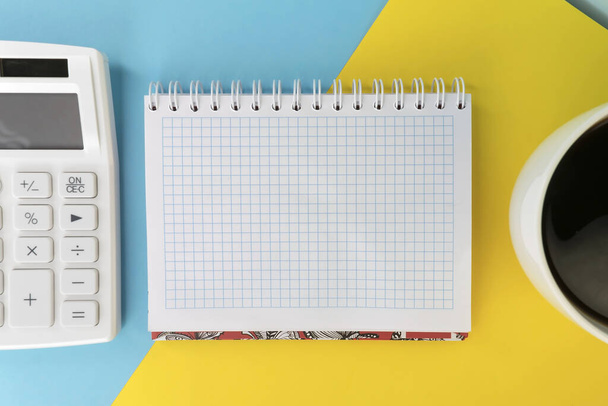 Op een kleurrijke achtergrond een vierkant notitieblok tussen een witte rekenmachine en een kopje koffie. Begrip bedrijfsplanning - Foto, afbeelding