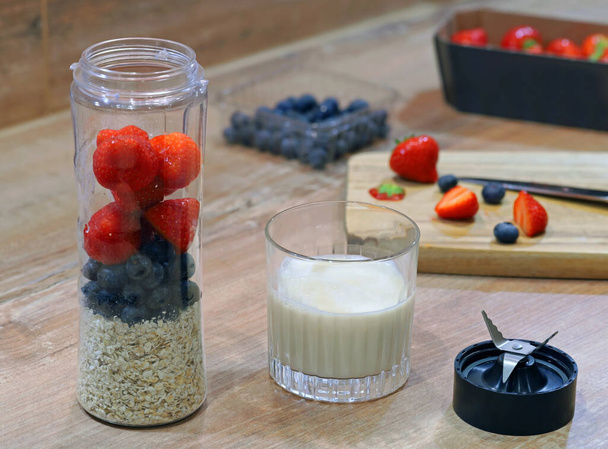 Smoothie mixer gevuld met vers gezond fruit en havermout, klaar om te mengen met melk op houten tafel - Foto, afbeelding