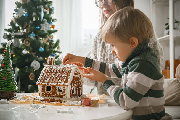 Child with mom decorating christmas gingerbread house together, family activities and traditions on Christmas and New Year's Eve - Foto, immagini