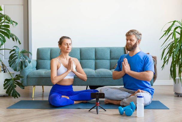 Photo of a couple meditating at home with online yoga tutorial. - Photo, Image