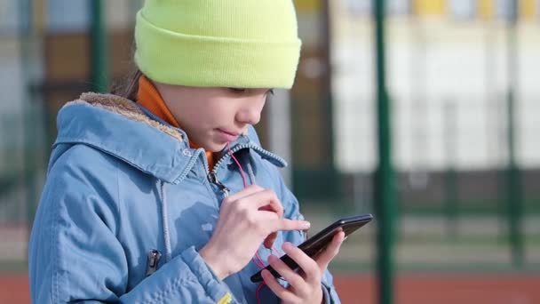 Teenagermädchen wählt Musik per Smartphone-App aus, steckt sich einen Kopfhörer ins Ohr und genießt die Musik. - Filmmaterial, Video