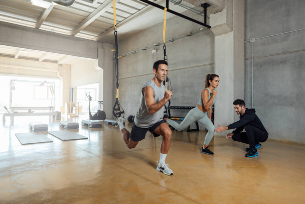 Γυμναστής γυμναστικής εκπαιδεύει άνδρες και γυναίκες να κάνουν lunge άσκηση σε ένα γυμναστήριο. - Φωτογραφία, εικόνα