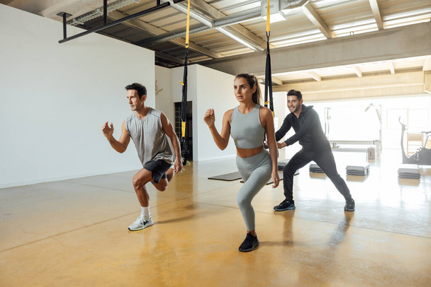 Sportowy mężczyzna i kobieta pociąg longe ćwiczenia z pętli funkcjonalnych w siłowni. - Zdjęcie, obraz