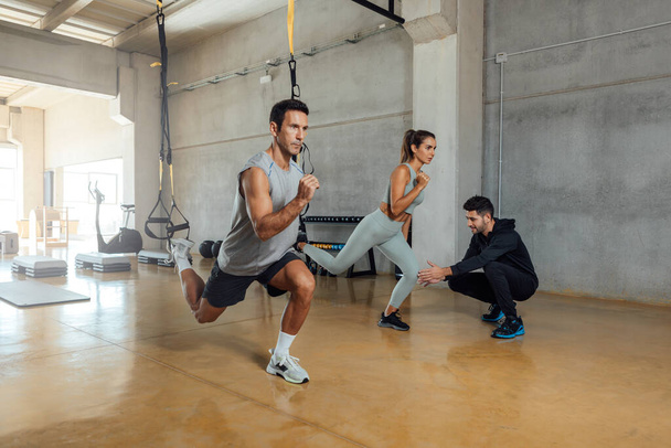Fitnesstrainerin trainiert Mann und Frau für Ausfallgymnastik im Fitnessstudio. - Foto, Bild