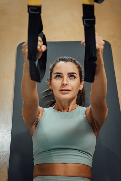 Porträt einer motivierten hübschen Frau beim Training im Fitnessstudio mit Aufhängevorrichtungen.  - Foto, Bild