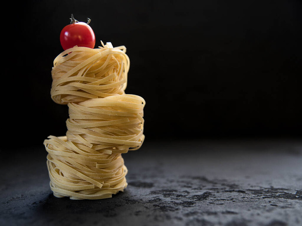 Raw tagliatelle pasta  and tomato on the black concrete background with a copy space .  - Photo, Image