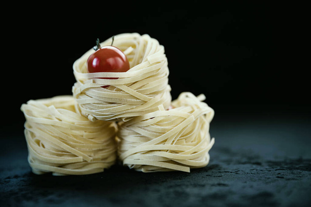Raw tagliatelle pasta  and tomato on the black concrete background with a copy space .  - Photo, Image