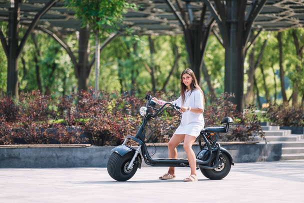 Молодая красивая женщина и электрический скутер, экологический транспорт - Фото, изображение