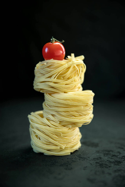 Raw tagliatelle pasta  and tomato on the black concrete background with a copy space .  - 写真・画像
