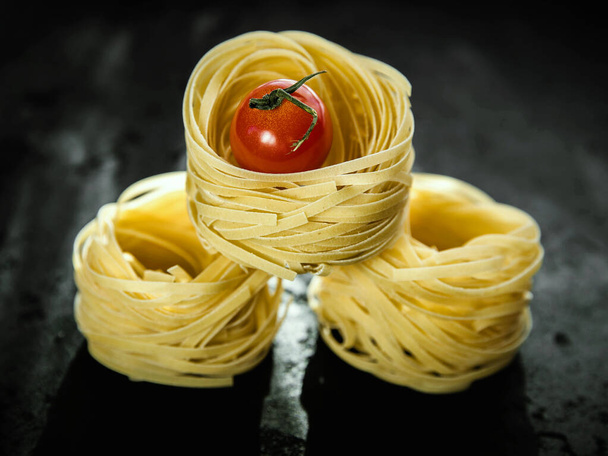 Raw tagliatelle pasta  and tomato on the black concrete background with a copy space .  - Foto, Bild