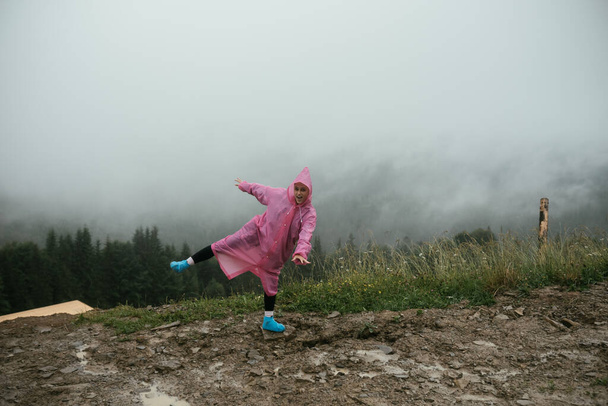 Привлекательная туристка в розовом плаще стоит на горе - Фото, изображение