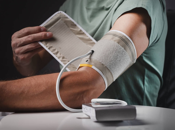 Blood pressure monitoring and checking. Man closeup putting on cuff on hand for heart health checkup at home - Φωτογραφία, εικόνα