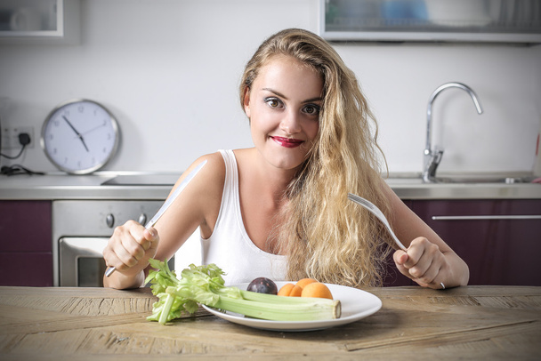 Blonde girl sitting at a kitchen counter ready to eat her meal - Photo, image