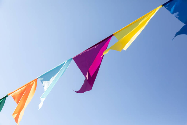 Γιρλάντα από πολύχρωμες τριγωνικές σημαίες που αναπτύσσονται στον άνεμο στο φόντο του γαλάζιου ουρανού. Γιορτή πάρτι. Γιορτινή διάθεση - Φωτογραφία, εικόνα