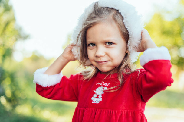 Christmas in july. Child waiting for Christmas in wood in summer. portrait of little girl in red dress decorating christmas tree. winter holidays and people concept. Merry Christmas and Happy Holidays - Fotoğraf, Görsel
