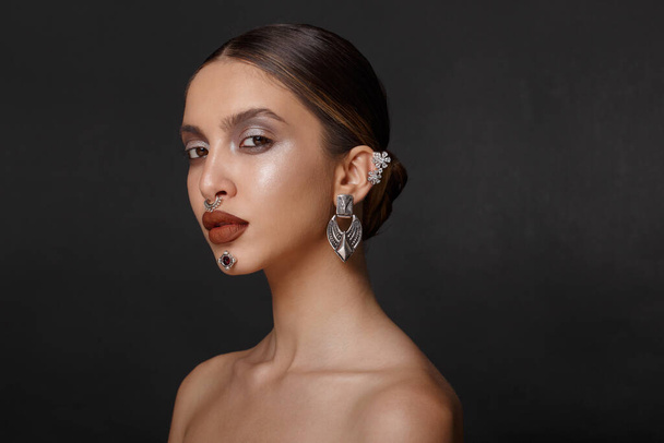 Closeup portrait of a girl with makeup, pose in profile with bare shoulders, jewelry, over black background. - Photo, Image