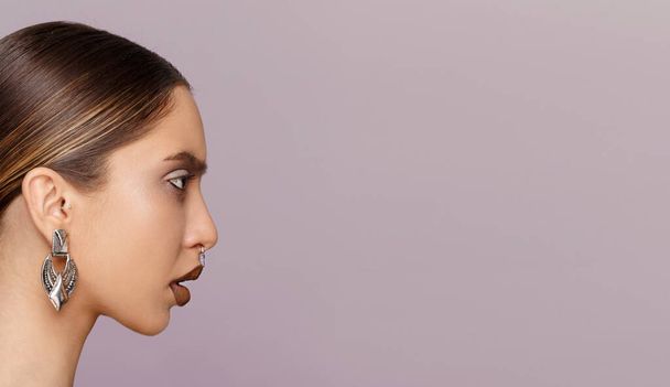 Profil Schönheit Porträt eines Mädchens mit Make-up und Schmuck aufgetragen, über violettem Hintergrund. Raum für Text. - Foto, Bild