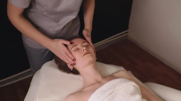 Kobieta masażystka ugniatająca zdrową głowę masaż twarzy relaksujący profesjonalną terapię olejkiem do rąk. Dziewczyna leżąca kanapa stół odpoczynku dostaje rubdown spa salon pielęgnacji ciała koncepcja, powolne leczenie ruchu - Materiał filmowy, wideo